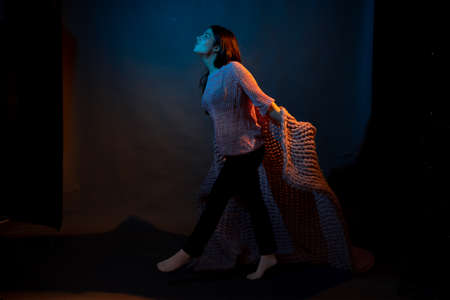 Girl in pink sweater with pink plaid on a dark background with colored lightの写真素材