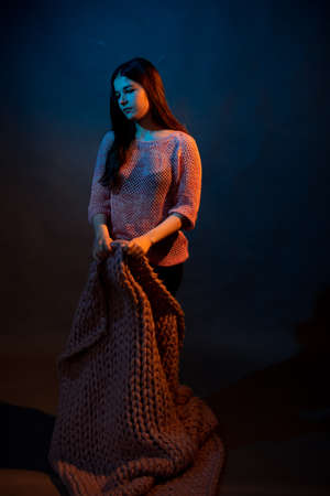 Girl in pink sweater with pink plaid on a dark background with colored lightの写真素材