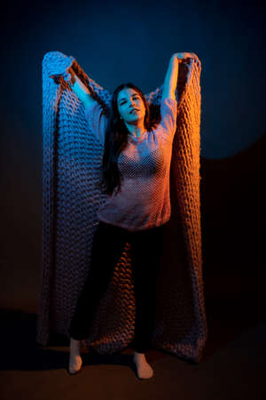 Girl in pink sweater with pink plaid on a dark background with colored lightの写真素材