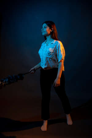 Girl in white shirt with dust brush on a dark background with colored light