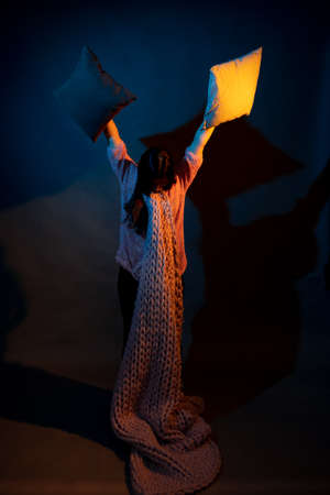 A girl in a pink sweater holds pillows illuminated by yellow and blue lightの写真素材
