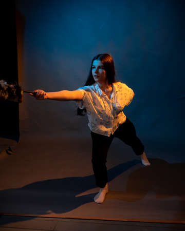 Girl in white shirt with dust brush on a dark background with colored lightの写真素材