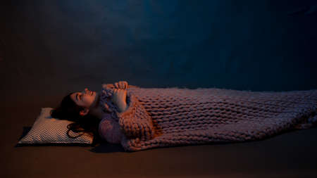 The girl lies on the floor, covered with a pink plaid, illuminated by a warm lightの写真素材