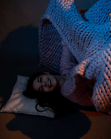 The girl lies on the floor, covered with a pink plaid, illuminated by a warm lightの写真素材
