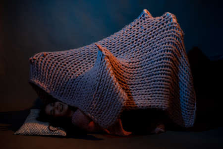 The girl lies on the floor, covered with a pink plaid, illuminated by a warm light