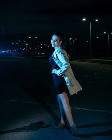 Girl at night in the parking lot in a beige coat against the background of lanternsの写真素材