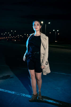 Girl at night in the parking lot in a beige coat against the background of lanternsの写真素材