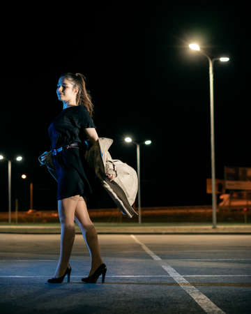 Girl in beige coat and dress against the backdrop of the night cityの写真素材