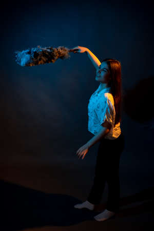 Girl in white shirt with dust brush on a dark background with colored lightの写真素材
