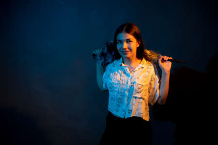 Girl in white shirt with dust brush on a dark background with colored lightの写真素材
