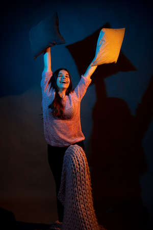 A girl in a pink sweater holds pillows illuminated by yellow and blue lightの写真素材