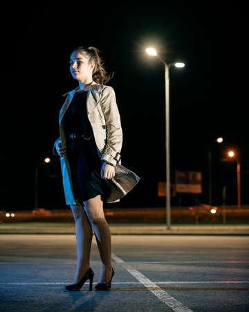 Girl in beige coat and dress against the backdrop of the night cityの写真素材