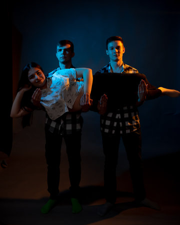 Two guys in a plaid shirt are holding a girl on a dark background in a studio with multicolored...