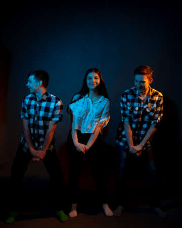 Two guys in plaid shirts and a girl dancing on a dark background, illuminated by blue and yellow light.の写真素材