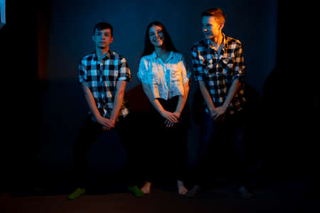 Two guys in plaid shirts and a girl dancing on a dark background, illuminated by blue and yellow light.の写真素材