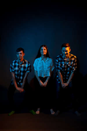Two guys in plaid shirts and a girl dancing on a dark background, illuminated by blue and yellow light.の写真素材