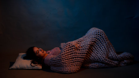 The girl lies on the floor, covered with a pink plaid, illuminated by a warm lightの写真素材