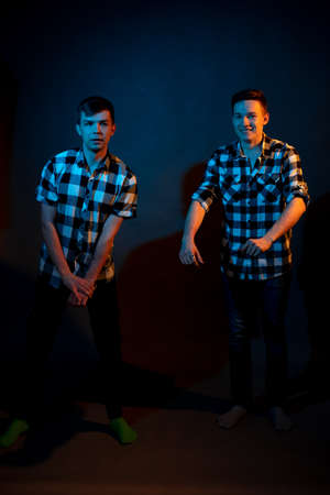 Two guys in a plaid shirt on a dark background with multicolored lighの写真素材