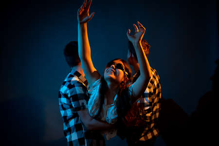 Two guys in a plaid shirt are holding a girl on a dark background in a studio with multicolored light.の写真素材