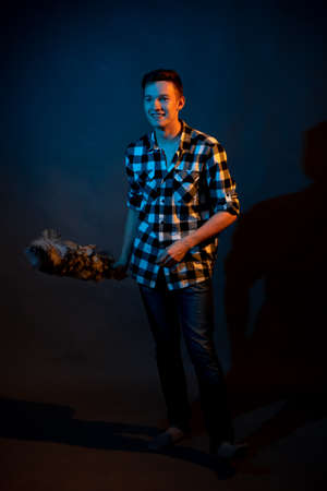 A guy in a plaid shirt with a dust brush on a dark background illuminated by blue and yellow lightの写真素材