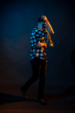 A guy in a plaid shirt with a dust brush on a dark background illuminated by blue and yellow lightの写真素材