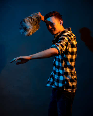 A guy in a plaid shirt with a dust brush on a dark background illuminated by blue and yellow light