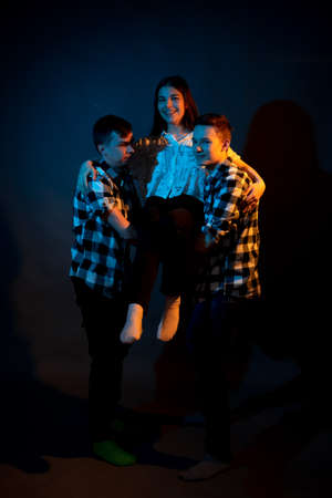Two guys in a plaid shirt are holding a girl on a dark background in a studio with multicolored light.の写真素材