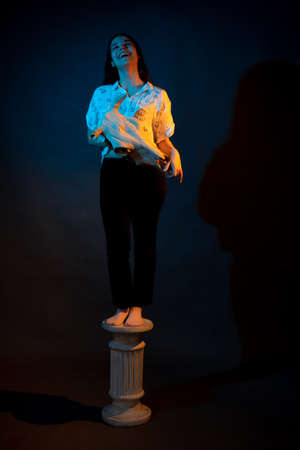 A girl stands on a Greek column with a bull skull in her hands illuminated by blue and yellow lightの写真素材