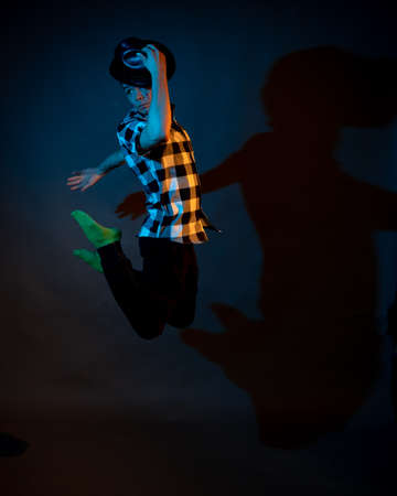 A young man in a plaid shirt jumps on a dark background illuminated by blue and yellow light.の写真素材