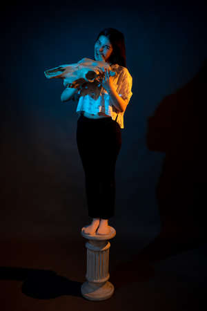 A girl stands on a Greek column with a bull skull in her hands illuminated by blue and yellow lightの写真素材