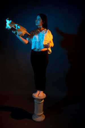 A girl stands on a miniature Greek column illuminated by multicolored lightの写真素材