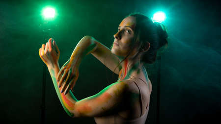 Girl with paint on her face against the background of smoke lit by cold lightの写真素材