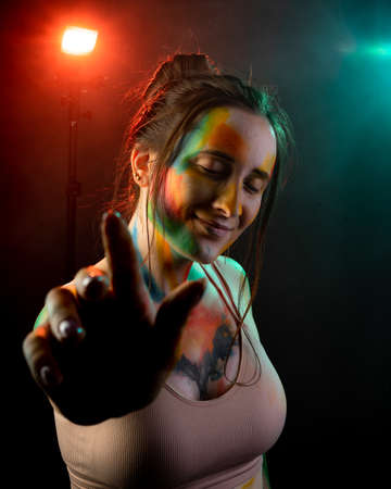 A girl with stains of paint on the body dances on a dark background with smoke illuminated by red and blue lightの写真素材