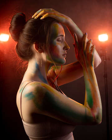 A girl with smears of paint on her face stands in smoke lit by warm lightの写真素材