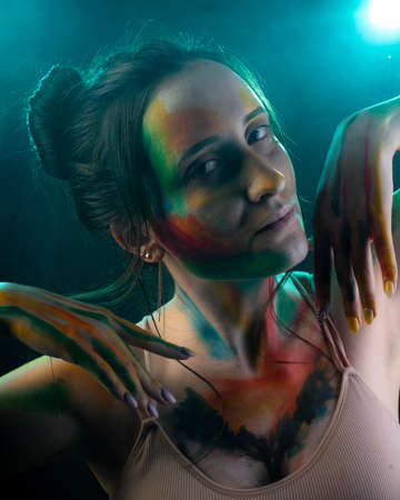 A close-up portrait of a girl with smears of paint on her face against the background of smoke illuminated by blue lightの写真素材