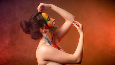 Girl with smears of paint on her face against a background of smoke illuminated by red lightの写真素材