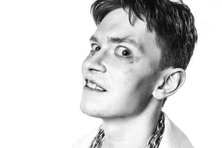 A mad lunatic with makeup and a chain wrapped around his neck screams against a white background....