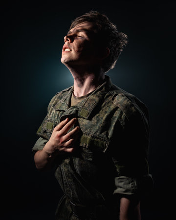 Portrait of a young soldier in uniform and combat coloring with bruises and scars on a black...