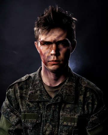 Portrait of a young soldier in uniform and combat coloring with bruises and scars on a black backgroundの写真素材