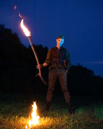 A guy dressed as Peter Pan stands with a burning torch against the night sky and dark forestの写真素材