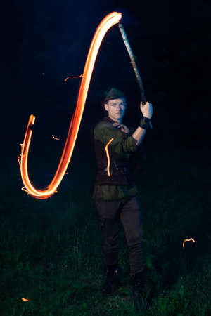 A guy in a Peter Pan costume twists a burning torch in his hands, which leaves a fiery trail, night...