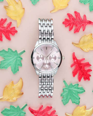Silver womens wristwatch with a pink dial on a pink background with multi-colored glass leaves.の写真素材