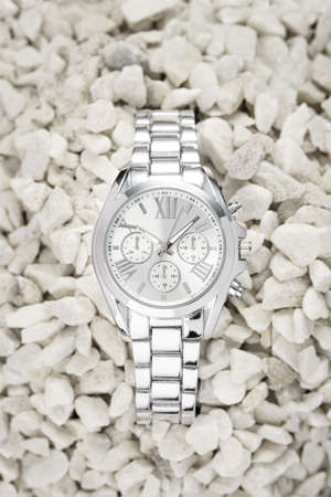 Silver watch with light dial buried in white pebblesの写真素材