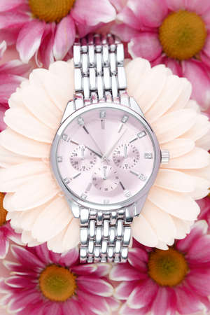 Womens wristwatch with silver strap and pink dial lies surrounded by purple flowersの写真素材