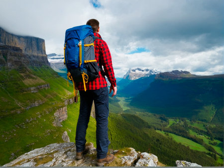 Hiker with a backpack standing on the edge of a cliff in the mountainsの素材
