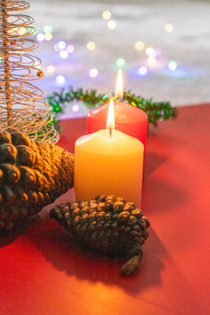 Christmas decoration with candles and pine cone on a red background with bokehの写真素材