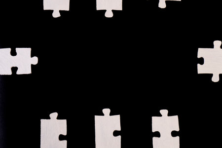 White jigsaw puzzle pieces isolated on black background with copy space.の写真素材