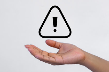 Hand holding exclamation mark isolated on white background. Hazard warning sign.の写真素材