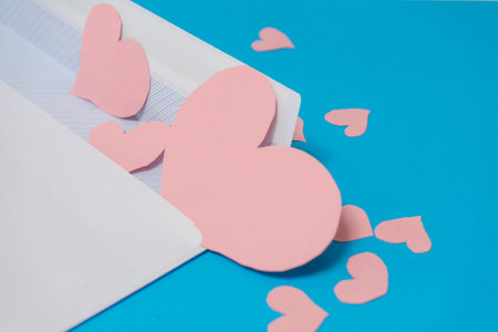 A white envelope with pink hearts on a blue background. Valentine's Day concept