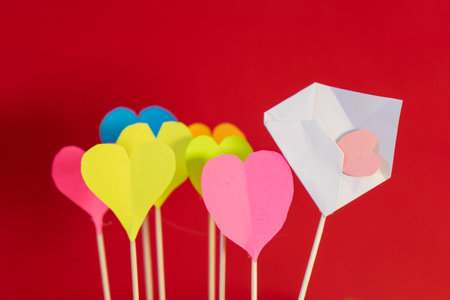 Colorful paper hearts on stick on red background, valentines day conceptの写真素材
